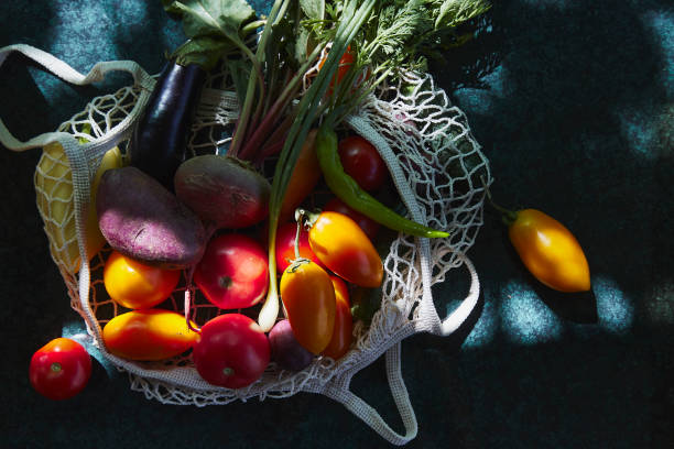 legumes frescos - tomates amarelos, berinjela, cebola, beterraba em saco de compras ecológicas sob sombras duras da moda com fundo de reflexão. preocupação ecológica. comida de vista superior. - onion carrot vegetable reflection - fotografias e filmes do acervo