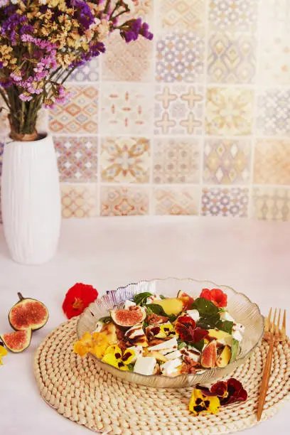 Vegetarian salad with feta, mango, edible flowers, figs, peach, basil on ceramic tile background with bouquet of dryflowers