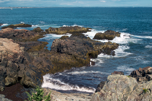 Looking out at the rocky coastline of the atlantic ocean, along marginal way in ogunquit maine, showing deep blue waves crashing on rocks.