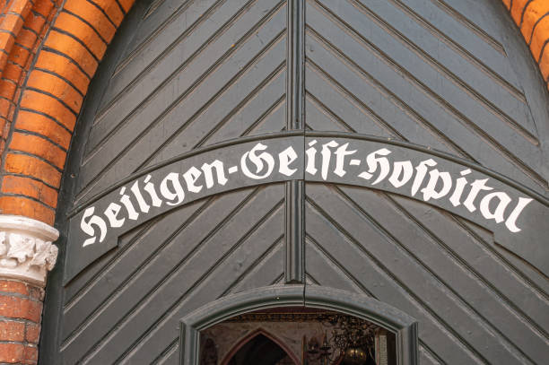 Germany, Lubeck - July 13, 2022: Historic Heiligen Geist Hospital main entrance has its name written in white on black door framed by red brick arch. Holy Spirit