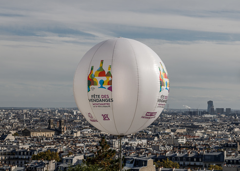 Montmartre grape Harvest Festival 2022, the 18th celebrates equality. A white balloon covered with the logos of the event in front of a blurred view of Paris