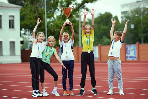 A boys and girls celebrating a victory. Motivated children team rising hands up. Happy kids playing sports. Concept of win, sport, studying, achievements, success,. teamwork, friendship and support