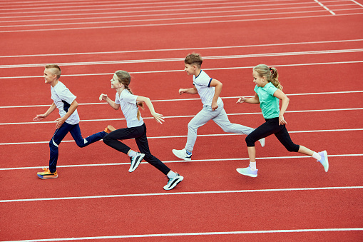 Group of children running on treadmill at the stadium or arena. Little fit boys and girls in sportswear training as athletes outdoor. Concept of sport, fitness, achievements, studying, goals, skills
