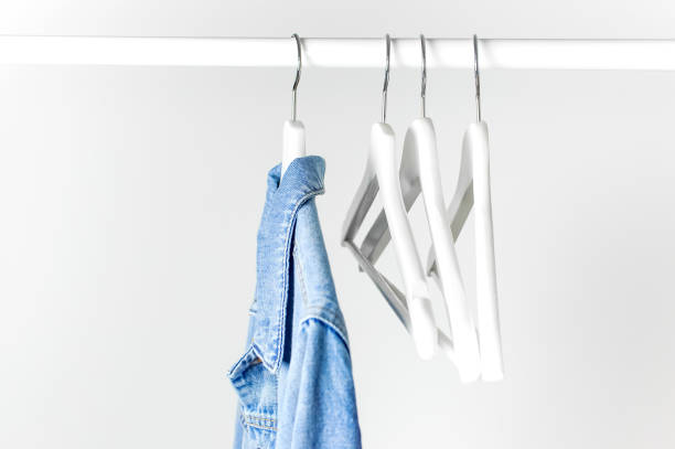 istock Blue denim jacket on white wooden coat hanger on a rod against light gray wall flat lay copy space. Denim, fashionable jacket, women's or men's trend clothing, fashion background. Store concept, sale 1431415512
