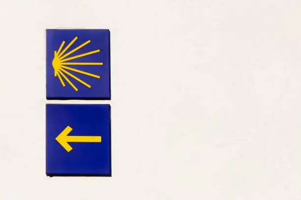 Pilgrims shell and yellow arrow, symbols of the  Camino de Santiago. White painted wall background. Copy space on the left.