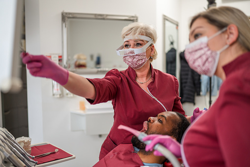 Una dentista caucásica y su asistente dental con un paciente masculino en el consultorio del dentista photo