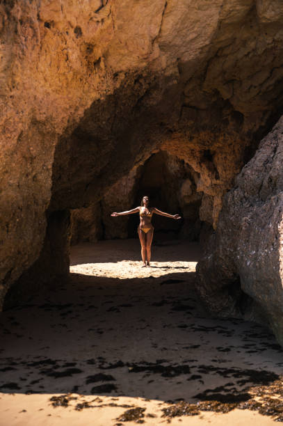 istock Carefree woman standing in cave on sandy beach 1431425340