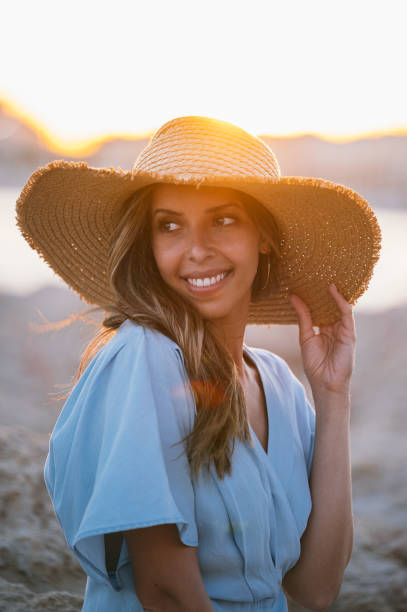 istock Smiling stylish woman resting on sandy shore at sunset 1431425460
