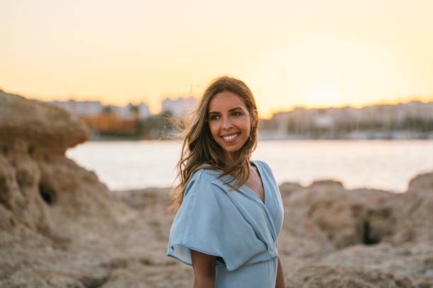 istock Smiling stylish woman resting on sandy shore at sunset 1431425461