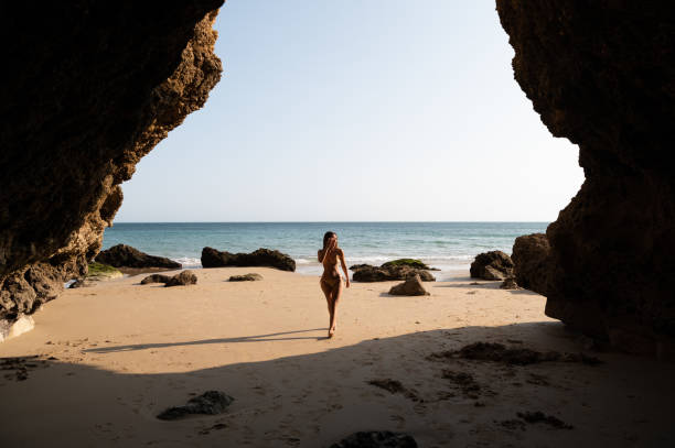 istock woman in bikini strolling on sandy seacoast near cliffs 1431427406