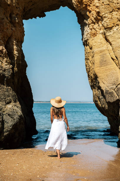 Unrecognizable woman walking on beach with rock stock photo