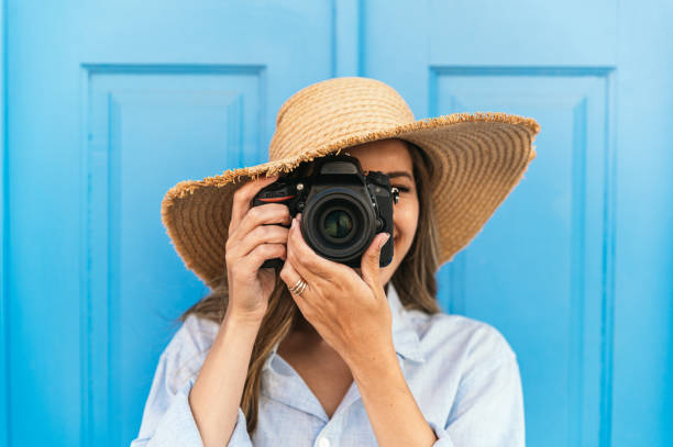Woman taking photo on camera in street Female traveler in straw hat taking picture on professional photo camera while standing near blue building on street during summer vacation in Lagos in Portugal algarve holiday stock pictures, royalty-free photos & images