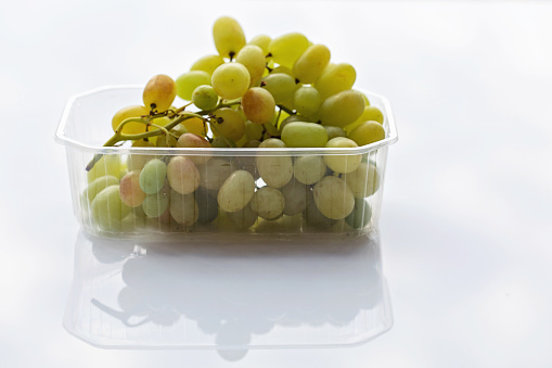 Green seedless grapes in a plastic container on a white surface