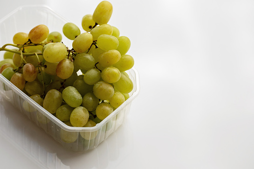 Green seedless grapes in a plastic container on a white surface