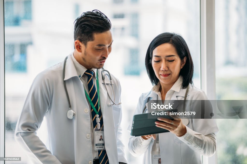 We should research more about this infection Shot of two Asian Chinese doctors using a digital tablet together in a hospital. Healthcare and Medicine concept. Doctor Stock Photo