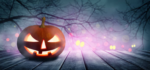 istock Spooky Halloween pumpkin, Jack O Lantern, with an evil face and eyes on a wooden table with a misty gray background. 1431436559