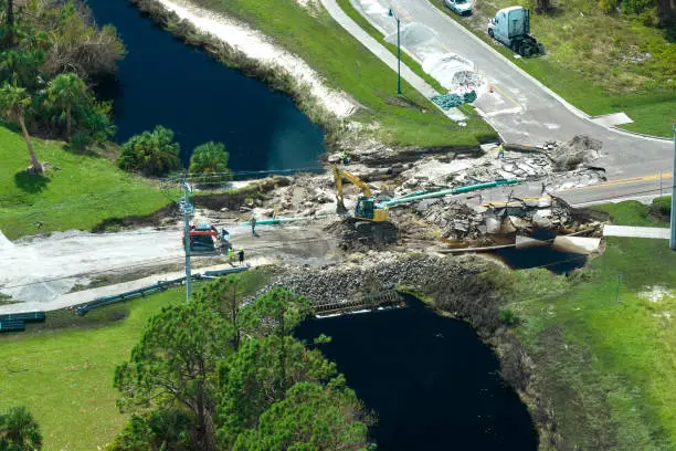 Photo of Aerial view of reconstruction of damaged road bridge destroyed by river after flood water washed away asphalt. Rebuilding of ruined transportation infrastructure