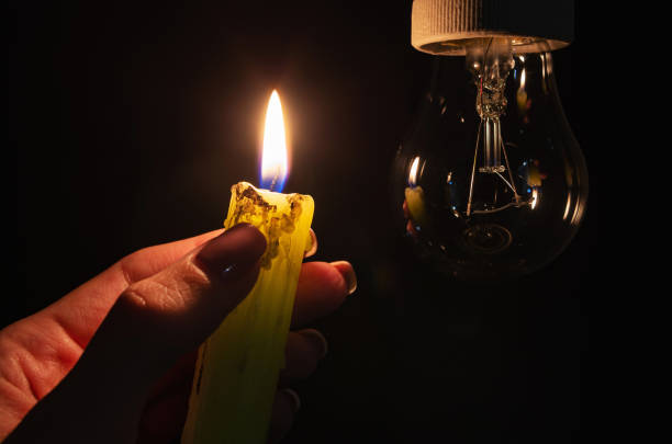 burning candle in complete darkness near a switched off light bulb at home. blackout, load shedding, electricity off, energy crisis or power outage, concept image. - fire match women flame imagens e fotografias de stock