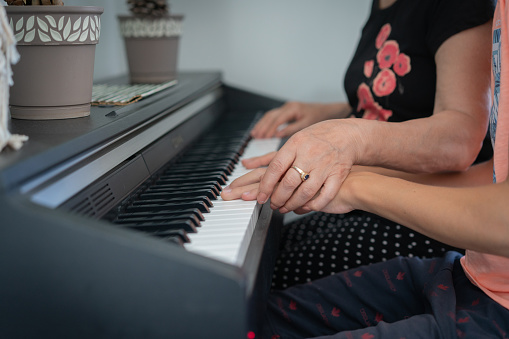 Close up senior woman teaching a young boy to play the piano with music notation.