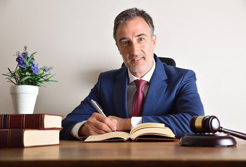 Well-suited lawyer signing on his office table with books and judge's gavel and isolated white wall background. Front view.