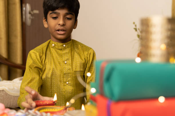 Young boy, kid, dressed up in ethnic lighting diya or lamp with smile expression pose for photo with family in background celebrating diwali Hindu festival Laxmi poojan stock photo