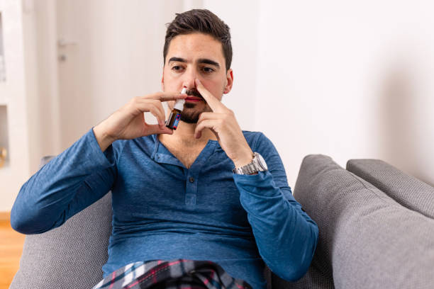 This always make me better A mid adult Caucasian man sitting on his sofa and applying nasal spray in his nose nasal spray stock pictures, royalty-free photos & images