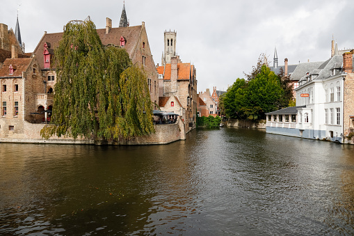 Bruges, Belgium - September 9, 2022: A complex of brick medieval buildings on the banks of the canal bend. You can see a fragment of a nearby stone bridge and people in an outdoor cafe by the water