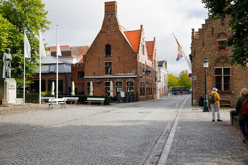 Bruges, Belgium - September 9, 2022: Brick historic houses on both sides of a cobblestone street. These buildings are seen here against the cloudy sky