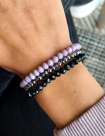 Three beada bracelets on womans wirst. Violet, black and silver colour.
