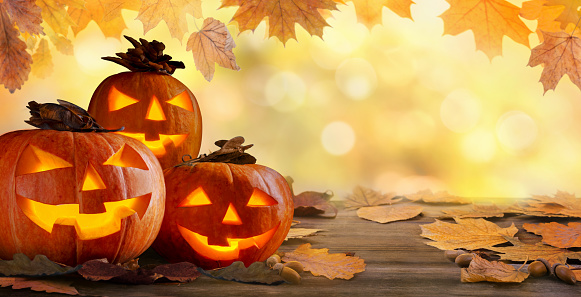 Halloween background. Jack O’ Lanterns Halloween pumpkins glowing on old rustic wooden table.