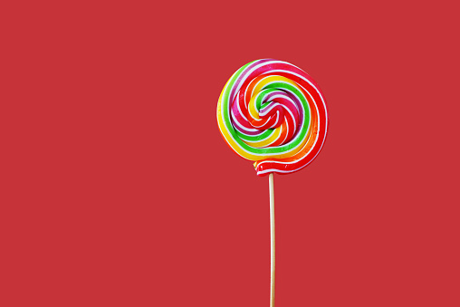 Close up view of a rainbow swirl lollipop on red background.