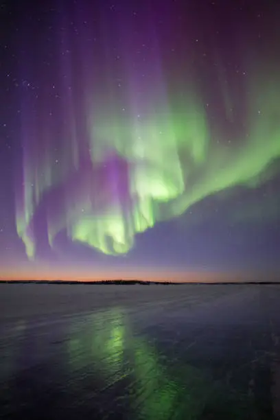 Photo of Active green and purple Aurora Borealis reflection on shiny winter ice road in Canada