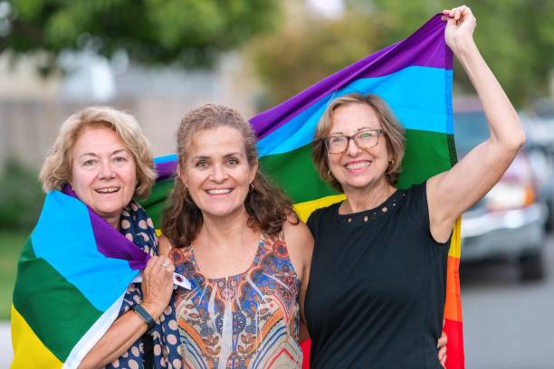 Smiling happy Mature and senior lesbian women posing holding a rainbow flag stock photo