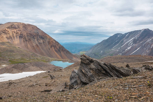 istock Dramatic landscape with old stone outliers and small mountain lake in sunlight under cloudy sky. Sharp rocks and small lake in high mountain valley with view to mountain vastness at changeable weather 1431512707