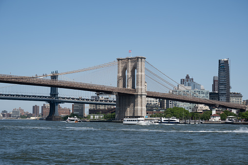 New York, NY, USA - June 4, 2022: The Brooklyn suspension tower of the Brooklyn Bridge seen across the East River, with the Manhattan Bridge and Brooklyn in the background.