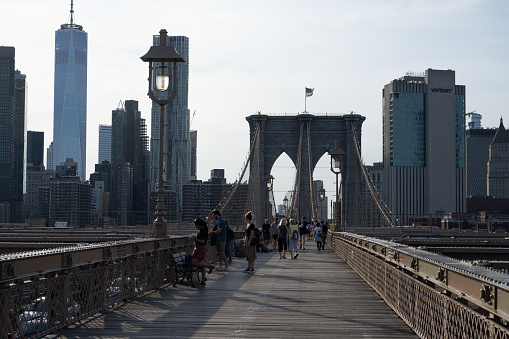 New York, NY, USA - June 6, 2022: People walking across Brooklyn Bridge, with Manhattan skyscrapers, including One World Trade Center, as the backdrop.