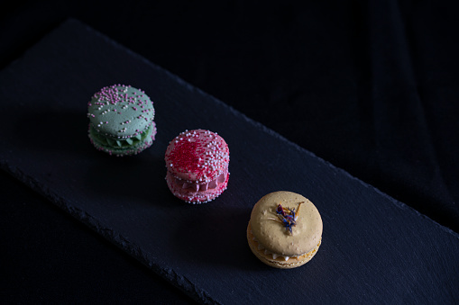 Set of three macaroons on a black slate plate. Passionfruit, strawberry and pistachio.
