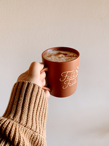 A Woman's Hand Holding a Hot Latté in a Terracotta-Colored Mug That Says 