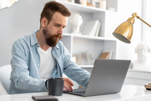 istock Stylish bearded man working on laptop from home sitting at the table 1431551718