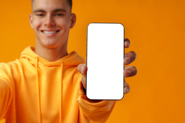 istock Smiling young man showing mobile phone blank white screen on yellow background 1431552771