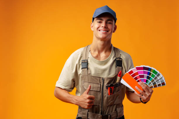 istock Handsome young worker in uniform holding paint samples palette on yellow background 1431555744