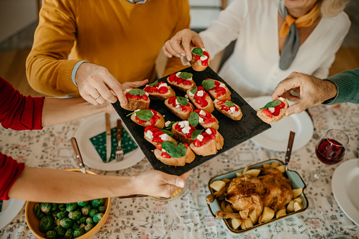 Smiling female holding a bruschetta plate and serving it during a Christmas lunch with her extended multigeneration family.