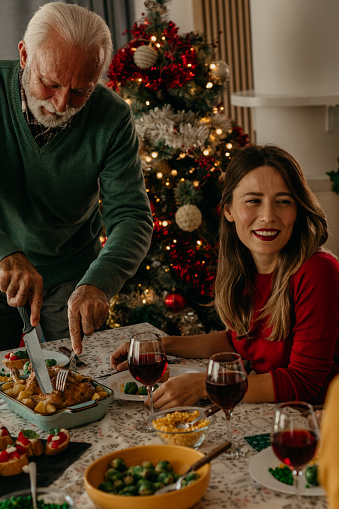 Cropped shot of a happy family having lunch together. Senior gray haired man cutting a turkey and serving it to his daughter.