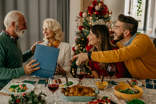 Happy two generation family having Christmas dinner together, senior man and woman received and holding a present in their hands.