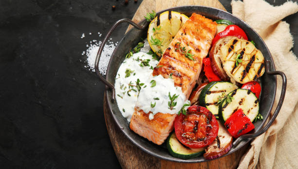 Salmon steak with vegetables and white sauce on dark background. stock photo
