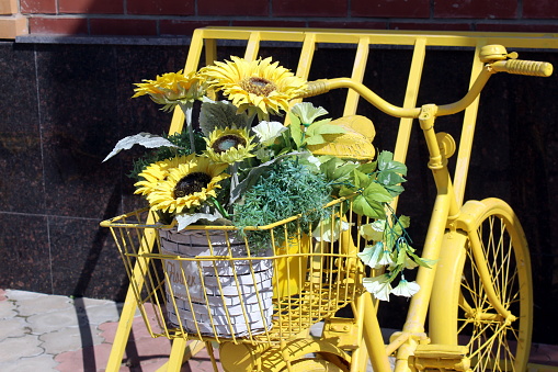 A yellow decorative bicycle with flowers stands in a parking lot on a summer day.