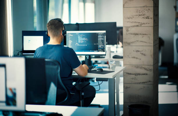 Software developer at the office. Closeup rear view of a young man coding on multiple computers web designer stock pictures, royalty-free photos & images
