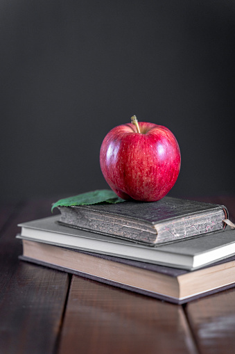 Red apple on books on a wooden table. Black background, copy space.