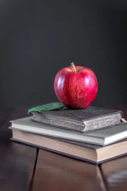 Photo of Red apple on books on a wooden table. Black background, copy space