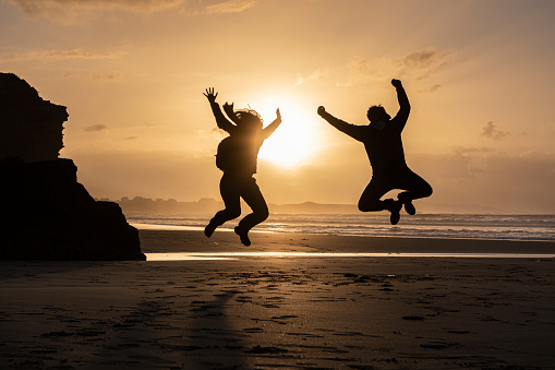 Sunset in the beach with a young couple silohuette jumping